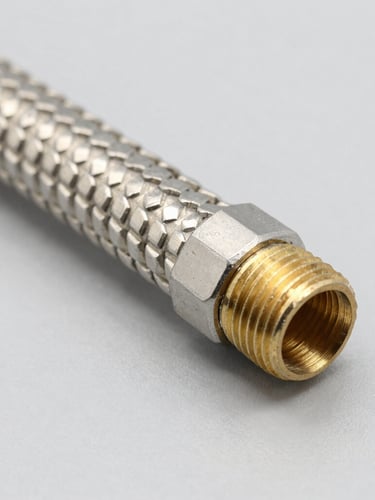 Sharp macro shot of stainless steel braided flexible hose, brass threads visible, bright studio lighting, neutral grey background, industrial focus