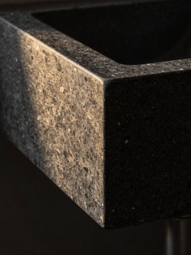 Macro architectural photograph of a sculpted porcelain sink with a perfect mitered joint, dramatic side-lighting, deep charcoal stone texture, razor-sharp focus, 35mm lens.