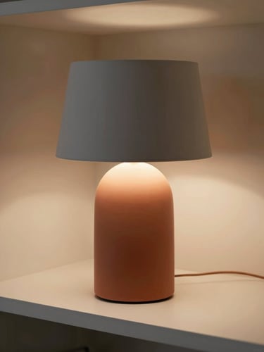 Close-up overhead shot of a modern table lamp on a warm white shelf, soft studio light, matte finish, minimal background, terracotta and gray tones