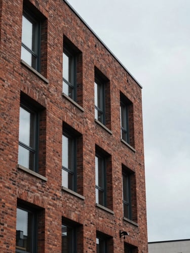 Overcast daylight shot of a modern brick multifamily building facade, focusing on structural textures and clean architectural lines, negative space on the right.