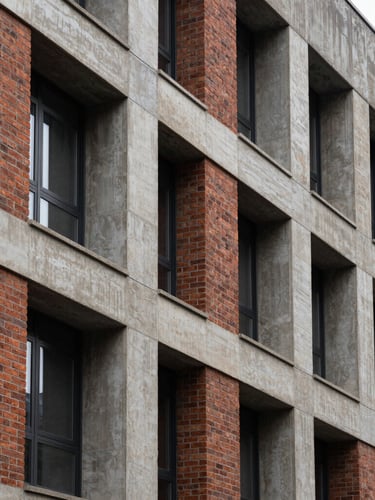 A high-contrast architectural crop of a brick and concrete multifamily building facade under overcast natural light, emphasizing structural textures and clean vertical lines.