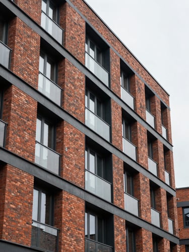 Tight architectural shot of a modern brick and steel multi-family building facade, overcast daylight, emphasizing structural textures and clean lines.