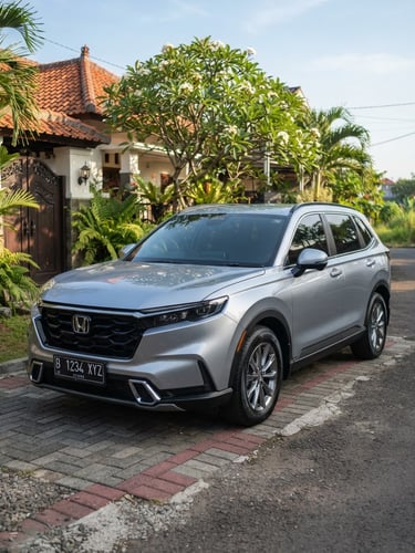 Three-quarter eye-level shot of a clean silver family SUV parked in a bright Indonesian residential driveway, warm morning sun, sharp focus, 35mm lens