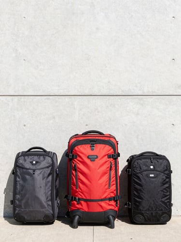 Crisp editorial travel photography of functional travel gear resting against a clean concrete wall, bright natural daylight, clean composition