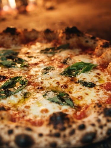 Extreme close-up of a perfectly blistered Neapolitan Margherita pizza, bubbling cheese, fresh basil leaves, and leopard-spotted crust, lit by warm firelight, shallow depth of field, 35mm.