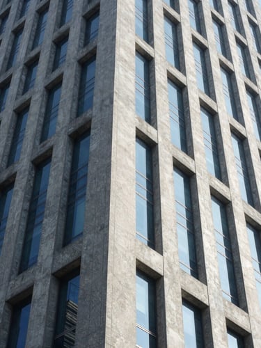 Low angle shot of a modern concrete and steel skyscraper facade in Jakarta, bright daylight, cool blue and slate tones, sharp architectural lines symbolizing strength