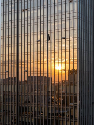 High-angle professional photograph of a modern glass skyscraper reflecting a golden sunset, sharp focus, 35mm luxury architectural photography