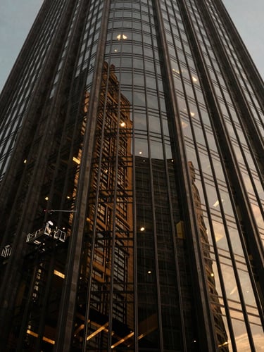 Low-angle architectural shot of a towering glass skyscraper under dramatic directional light, sharp reflections, professional cleaner visible at a distance on a high-end rig, luxury 35mm photography