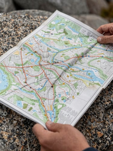 A close-up of hands gripping a worn topographic map over a granite rock, overcast daylight, sharp focus on the textured paper and weathered skin.