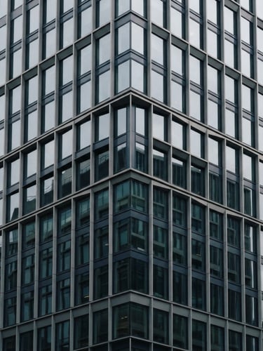 Architectural detail of a modern financial district building facade with geometric shadows, soft overcast light, muted navy and slate tones, 35mm.