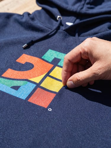 Close-up shot of hands carefully aligning a colorful DTF print on a navy blue cotton hoodie, bright natural daylight, warm color palette, sharp focus on fabric textures.