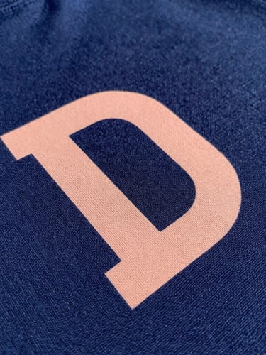 Close-up shot of rich navy fabric texture with a crisp peach-colored DTF print, natural daylight, sharp focus on thread detail, 50mm lens
