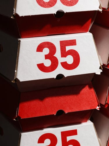 Close-up macro shot of clean stacked cardboard burger boxes with bold red branding, high-contrast studio lighting, deep charcoal shadows, sharp focus, 35mm