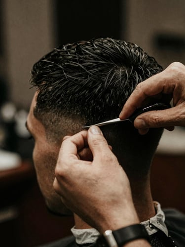 Close-up of a barber's hands performing a precise haircut, warm low-key ambient lighting, deep charcoal tones, shallow depth of field, 35mm