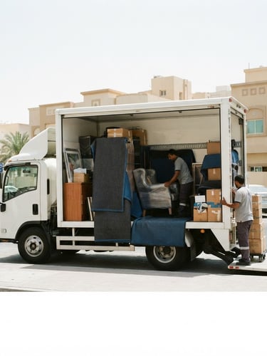 A clean white moving truck parked on a bright Abu Dhabi street, side view showing organized loading, thick protective blankets visible, bright natural daylight, 35mm photography