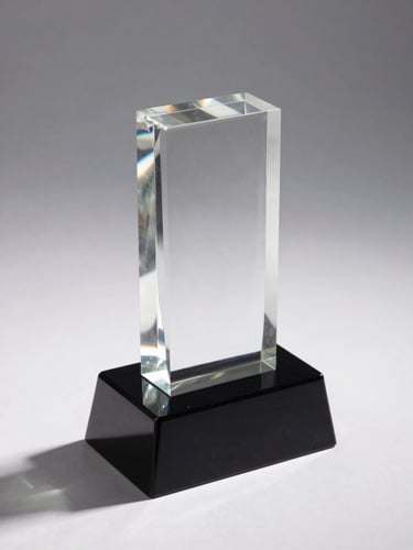 3/4 angled view of a crystal award block on a white studio surface, neutral backlight creating a prismatic internal glow through the transparent crystal, precision-engraved text visible on the front face, black rectangular base below