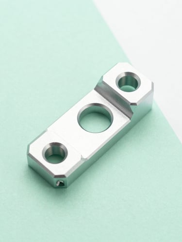 Overhead macro shot of a clean, millimeter-precise custom machined aluminum bracket resting on a soft pastel mint green surface under bright diffused daylight, sharp focus, 50mm