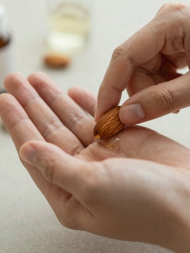 Soft natural light photography, extreme close-up of hands applying cold-pressed sweet almond oil, muted sage tones, shallow depth of field