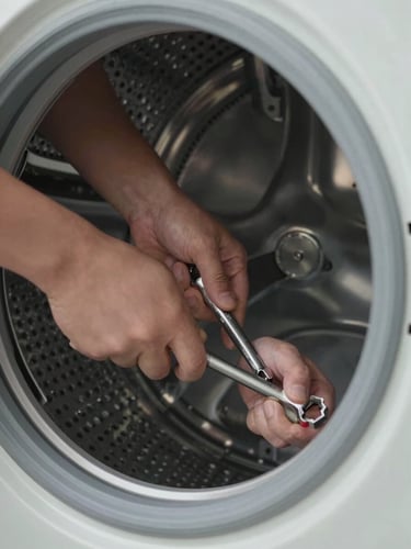 Extreme close-up of a technician's hands tightening a component inside a washing machine drum, a socket wrench gripped firmly, clean window light from the left casting crisp shadows on the metal housing, no faces visible