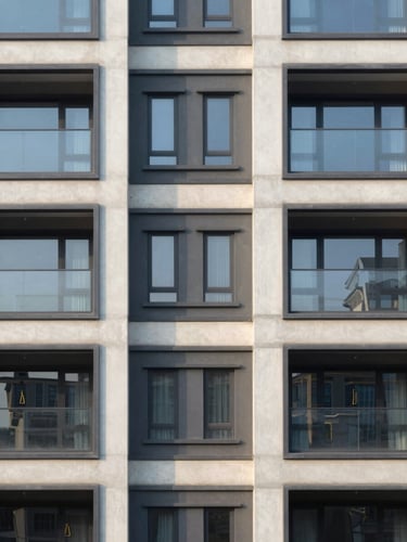 Straight-on elevation of a contemporary residential development facade, showing clean architectural lines, structured concrete panels, and large windows reflecting soft morning daylight.