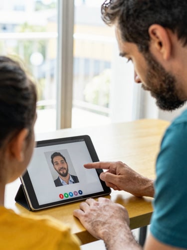 Candid medium close-up of a mentor and student analyzing a digital design on a tablet screen during a video call, bright natural window light, vibrant gold accents, 35mm