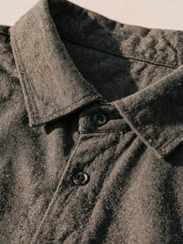 A tight macro shot of a charcoal heavy-weight cotton collar line and clean seams, warm directional afternoon sun casting soft shadows, showing fabric texture.