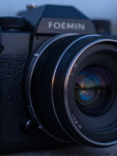 Macro close-up of a dark anodized aluminum camera housing with a precision optical lens reflecting subtle blue twilight, shallow depth of field, 35mm