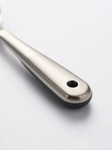 Close-up macro shot of a brushed stainless steel kitchen utensil handle and a smooth silicone edge, highlighting texture and material quality, bright minimalist product photography, clean natural daylight, soft shadows, crisp white background, 50mm