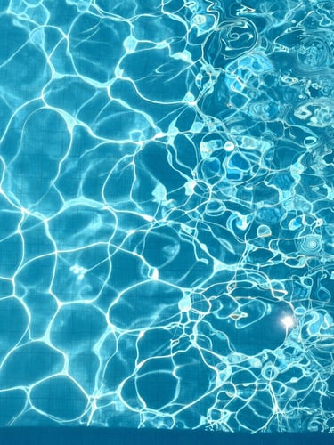 Top-down overhead shot of a pristine, crystal-clear swimming pool water surface under direct, bright high-noon sunlight, sharp clean shadows on pool tiles, highly detailed water texture.
