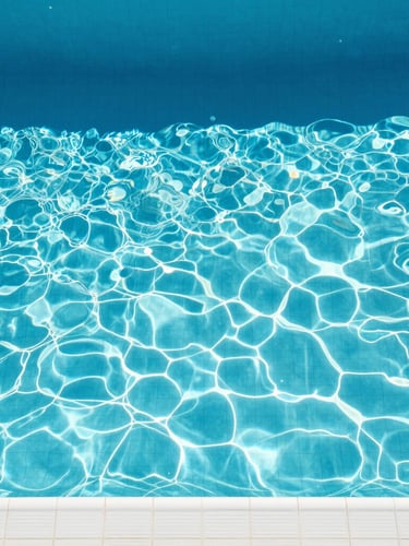 Top-down overhead shot of a swimming pool with crystal-clear cerulean water, clean white tiles, and sharp geometric shadows cast by high-noon direct sunlight