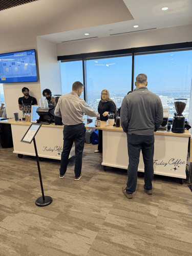 Customers ordering drinks at a Friday Coffee mobile espresso bar in a high-rise office with city views.