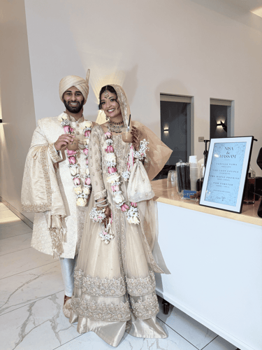A smiling bride and groom in traditional ivory wedding attire posing with drinks at their reception.