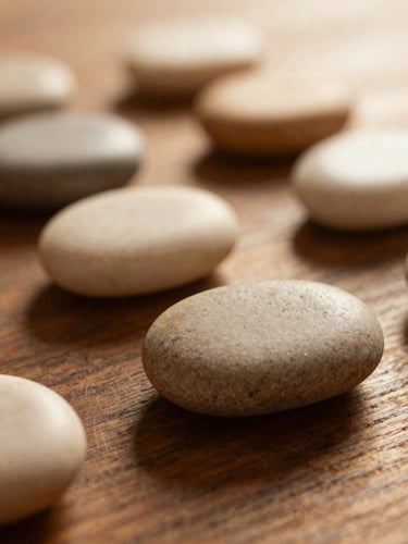 Close-up of smooth warm massage stones resting on a dark wood table, soft diffused golden-hour light, shallow depth of field, 35mm