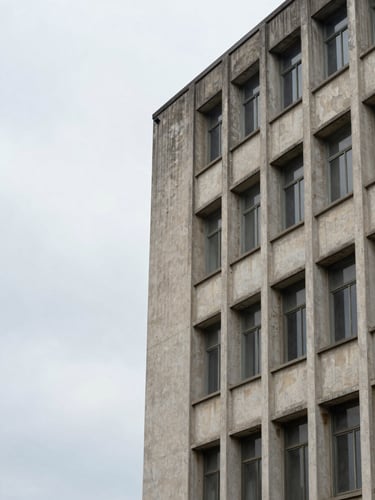 Low angle view of a weathered brutalist concrete building facade with rows of windows under a grey sky.
