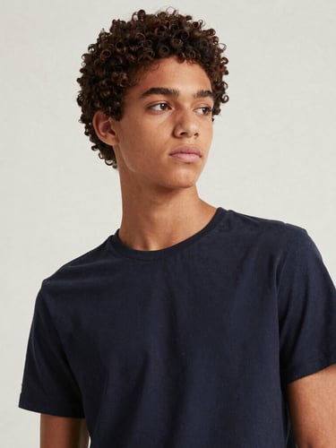 Editorial fashion portrait of a stylish Brazilian teenager looking thoughtful, clean minimalist background, soft natural daylight, rich muted tones, high-end magazine style.
