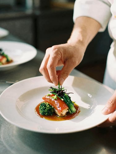 Close-up of chef's hands plating a vibrant dish in a warm kitchen, soft natural side daylight, shallow depth of field, 35mm film