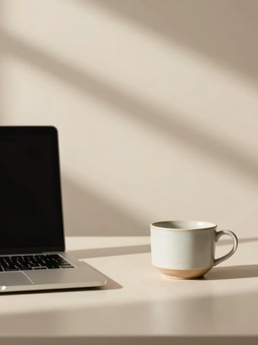 Minimalist workspace with soft morning shadows on a warm cream wall, a sleek laptop, and a single ceramic cup, overhead crop, elegant and calm.