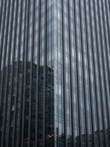 Sharp, linear, and symmetrical close-up of a glass-and-steel skyscraper facade reflecting an overcast gray sky, deep depth of field, high-contrast cool studio lighting.