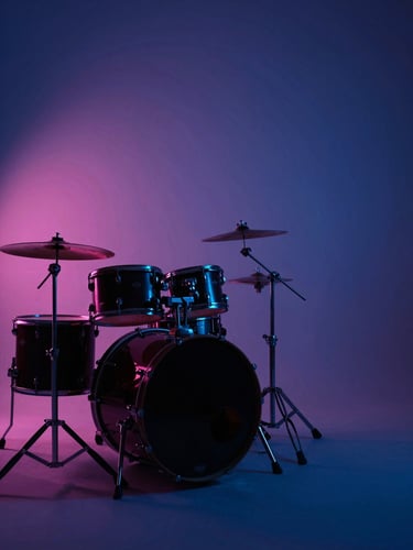 Wide atmospheric studio shot, a drum kit silhouetted in the left frame under deep blue and pink stage backlighting, moody high-contrast environment, drum hardware catching neon reflections, negative space on the right