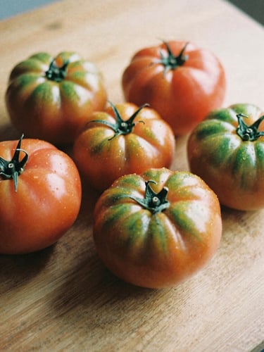 A close-up, warm editorial photograph of fresh heirloom tomatoes on a wooden prep table, soft Scandinavian daylight casting deep shadows, matte texture, 35mm film