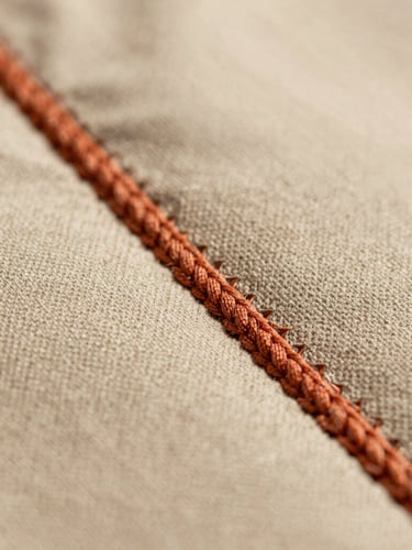 Extreme macro close-up of thick terracotta embroidery stitches on a soft sand cotton jacket, showing individual thread fibers and physical depth.