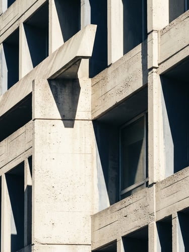 Macro architectural crop of a modern concrete building facade, sharp diagonal shadows, high-contrast daylight, desaturated navy tones, 50mm lens