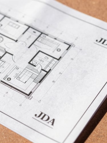 Close-up of clean, organized architectural blueprints and official JDA stamp documents resting on a warm terracotta surface under bright afternoon sunlight, 35mm lens