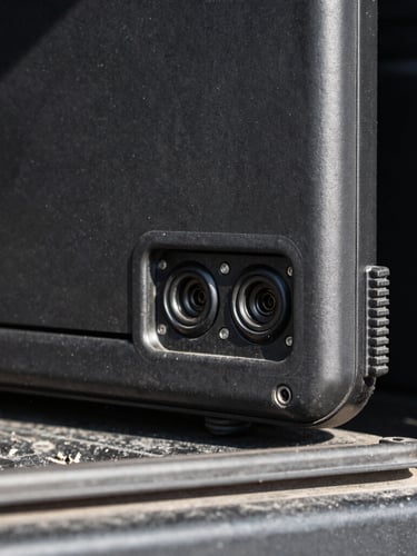 Close-up macro shot of a ruggedized matte-black laptop casing mounted inside a utility truck, harsh direct sunlight highlighting heavy-duty ports and sealed rubber gaskets, 35mm gritty industrial photography