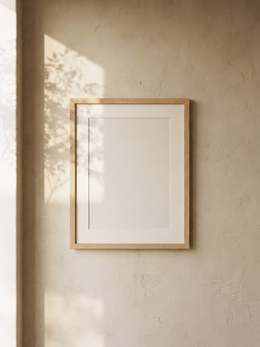 Straight-on architectural shot of an empty oak frame on a textured beige plaster wall, soft morning window light casting a gentle foliage shadow, 35mm
