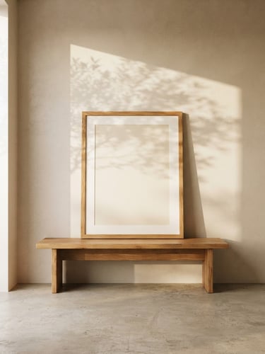 A straight-on architectural shot of a sunlit minimalist room, clean beige plaster walls, a large empty oak frame resting on a low wooden bench, soft morning light casting gentle shadows of olive leaves, 35mm photography