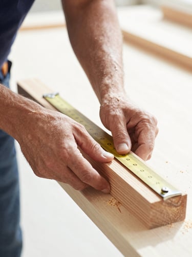 Close-up of a French carpenter hands carefully measuring a piece of light oak wood in a sunlit workshop, sawdust in the air, bright natural daylight, professional 35mm