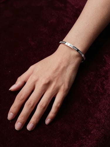 Elegant portrait of a woman's hand resting on a dark velvet surface, wearing a custom-engraved silver bracelet, soft dramatic side-lighting