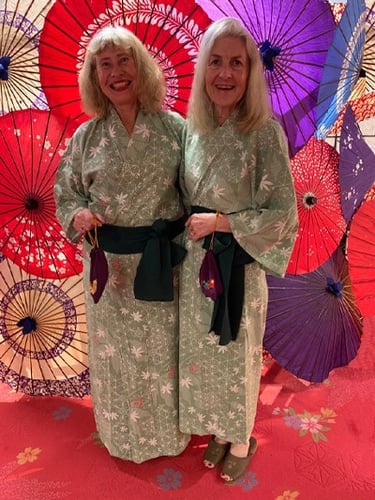 Two women wearing kimonos standing in front of a display of open parasols.
