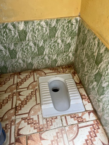 Squat toilet with tiles on floor and walls..